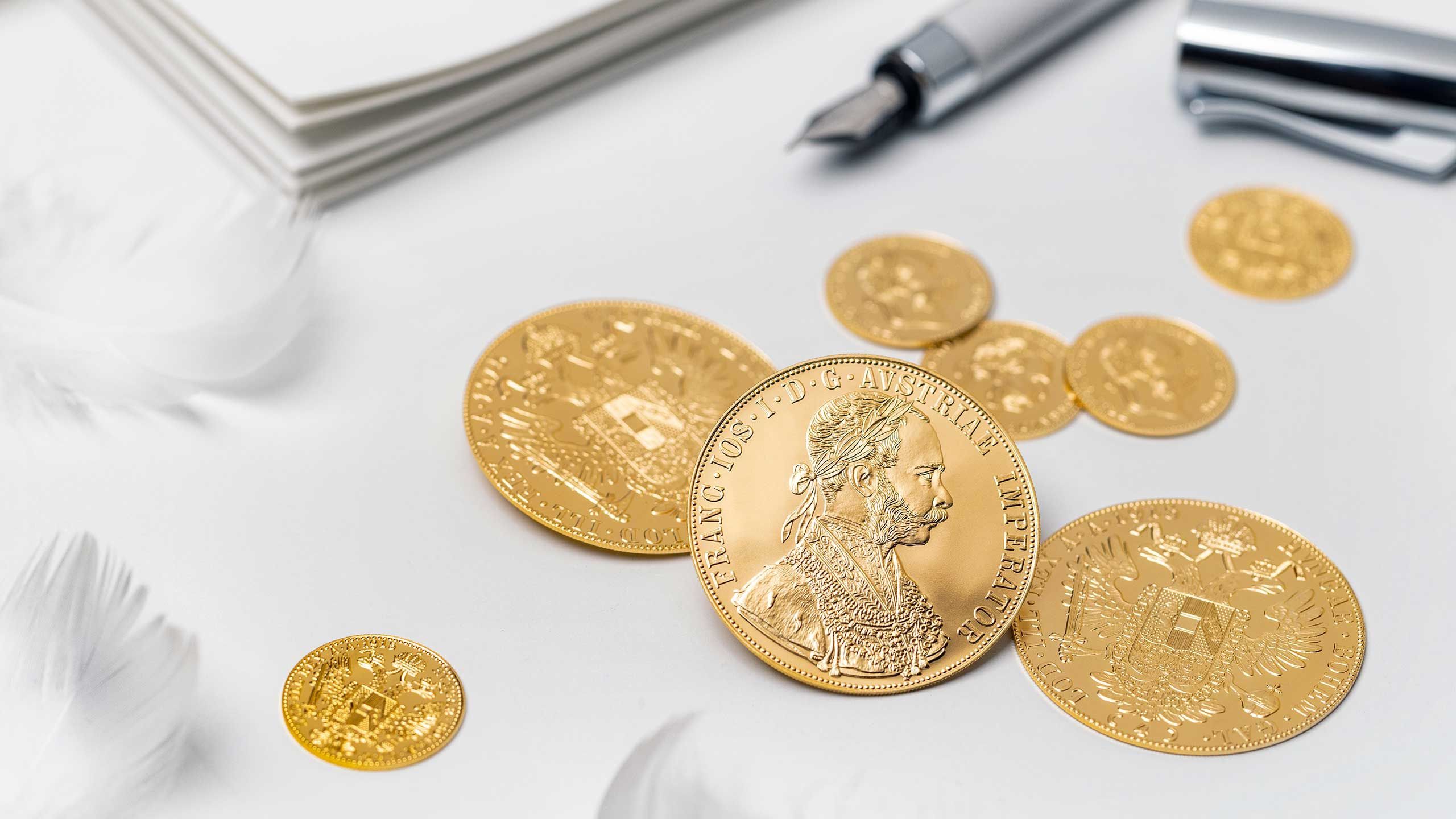 Gold coins from the Austrian Mint displayed on a white surface