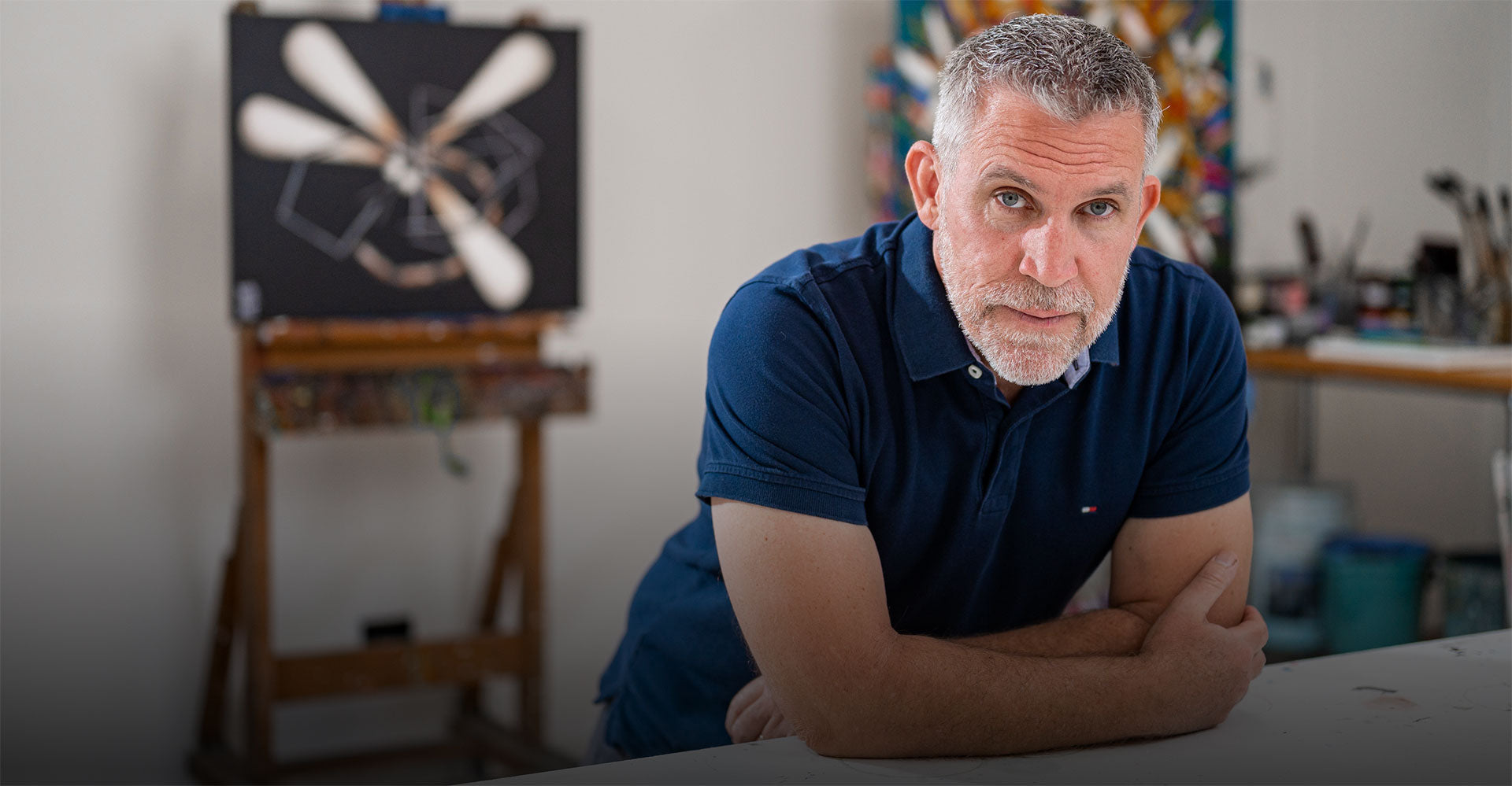 David Hart in his studio leaning on his desk with a black dragonfly painting in the background