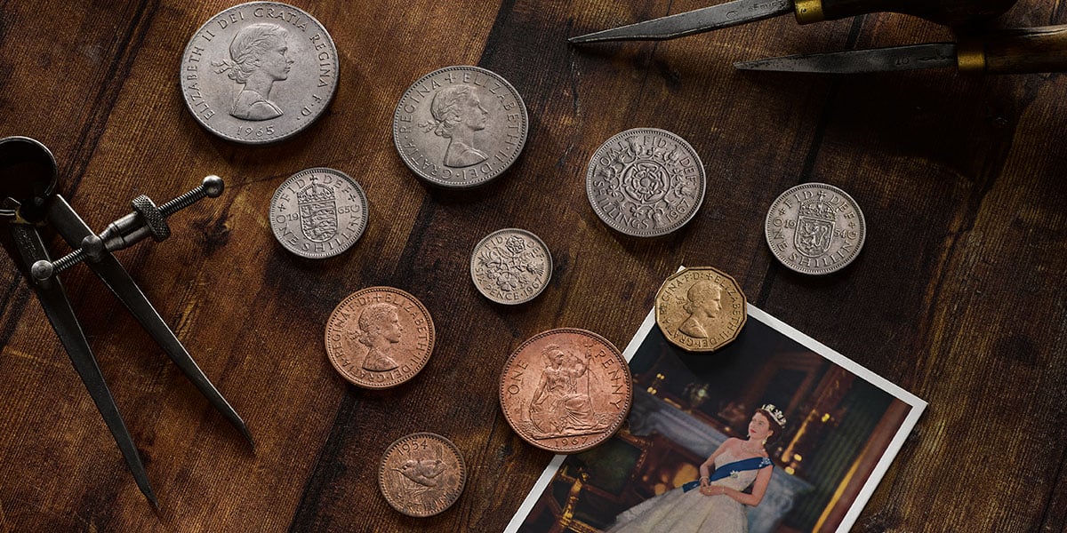 Collection of vintage coins produced by The Royal Mint on a wooden surface with a portrait photo of the Queen